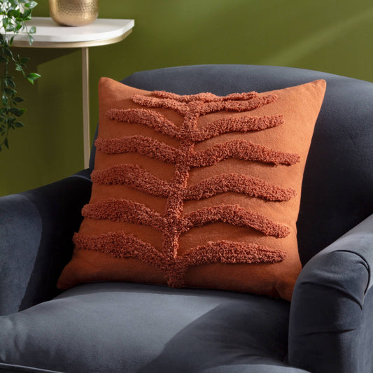 Orange textured leaf cushion on a grey armchair with a green wall in the background