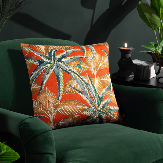 Jahi tropical cushion with bold green florals, gold leaves, and a hidden frog detail on a vibrant background, styled on a green velvet chair.