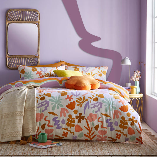 Colorful floral bedding on a bed in a room with a purple wall and gold mirror.
