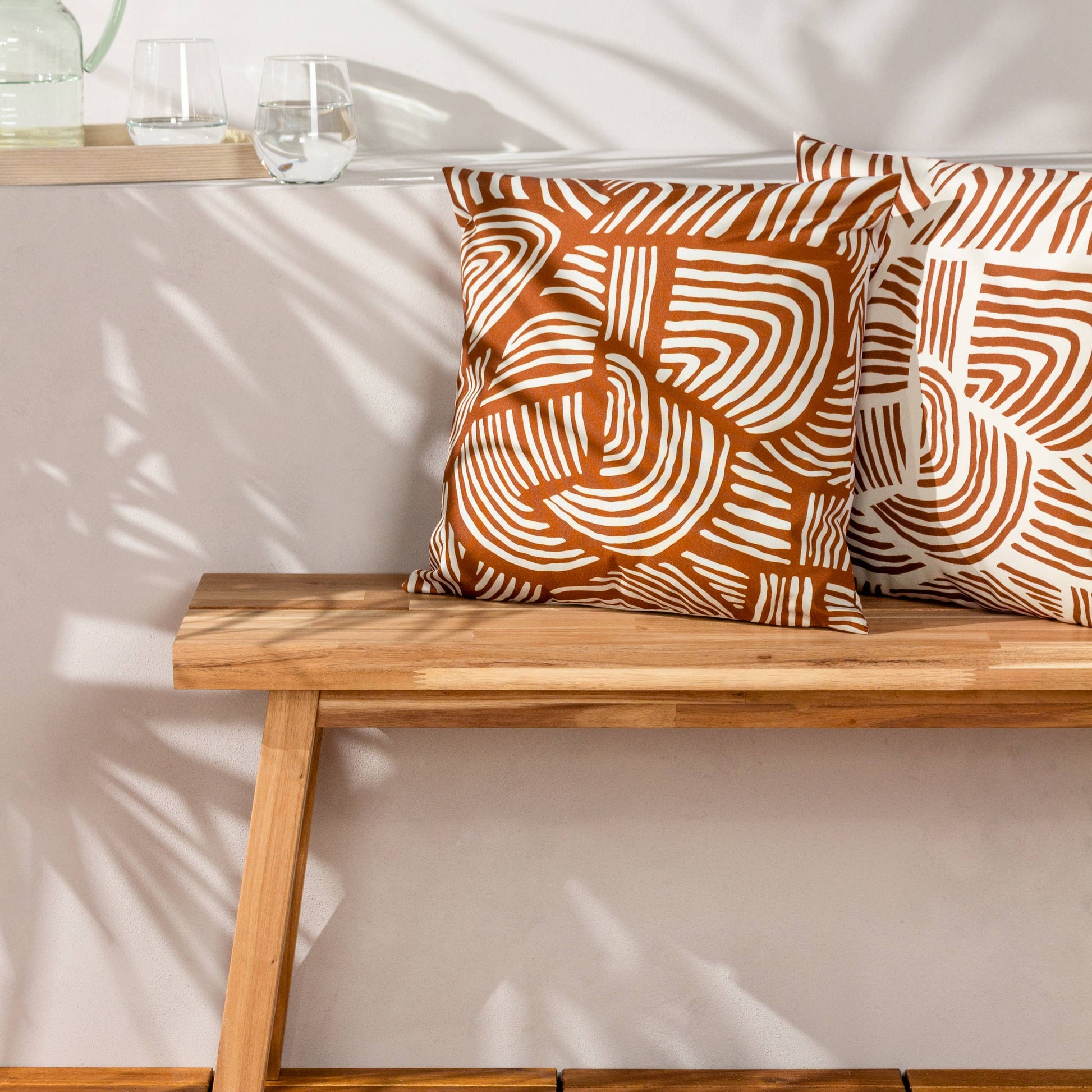 Wooden bench with dunes orange patterned cushions against a neutral wall