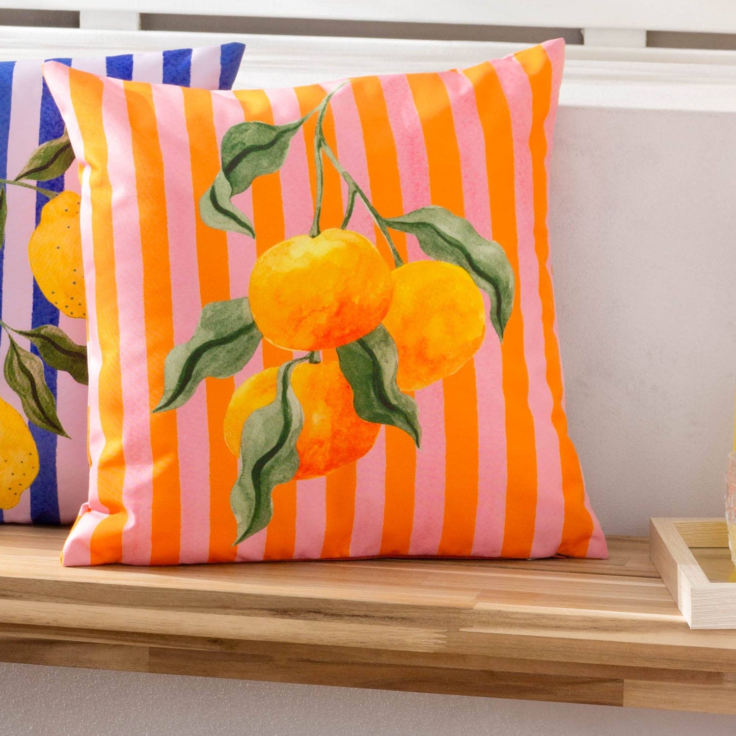 Orange and pink Striped cushion with fruit patterns, styled on a wooden bench.