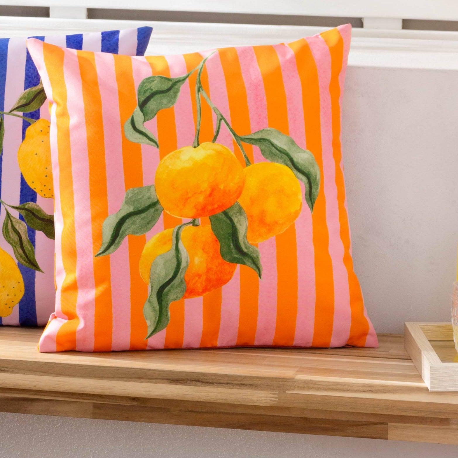 Orange and pink Striped cushion with fruit patterns, styled on a wooden bench.