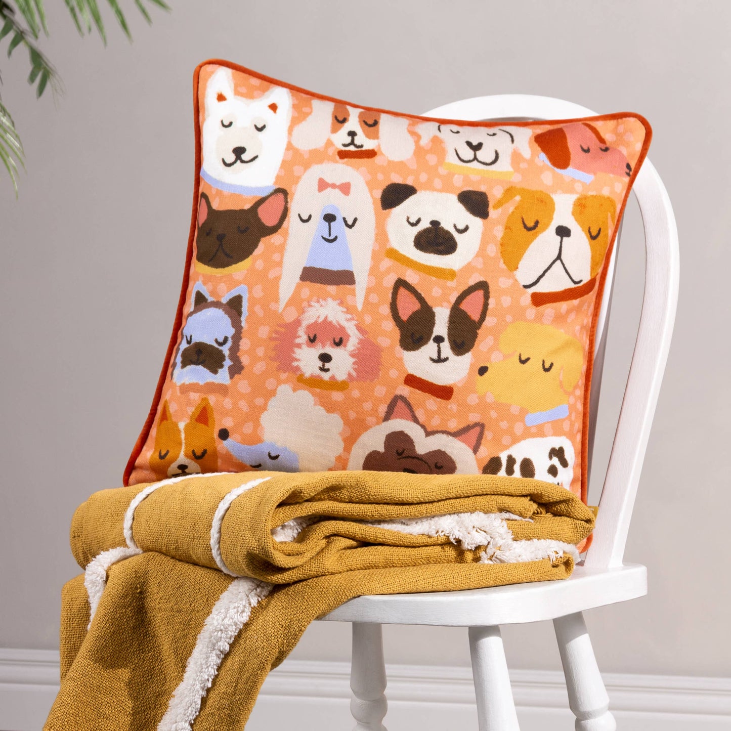 Decorative pillow with dog pattern on a white chair with a yellow blanket.