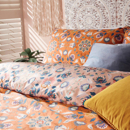 Floral scandi orange patterned bedding with colorful pillows on a bed.