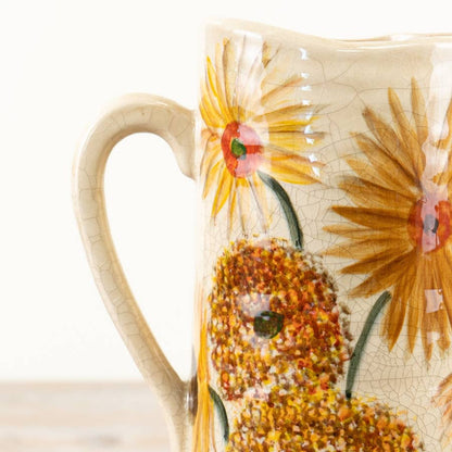 Close up of a tall ceramic pitcher with a sunflower botanical illustration and cream crackle glaze finish