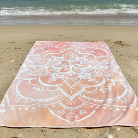 Orange ombre mandala beach towel on the sand with ocean waves in the background