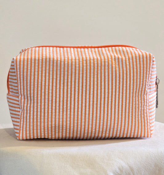 Striped fabric pouch with orange and white pattern on a light gray surface.