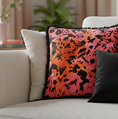 Maximalist animal print cushion with pink and orange background and black fringe trim on a beige sofa 